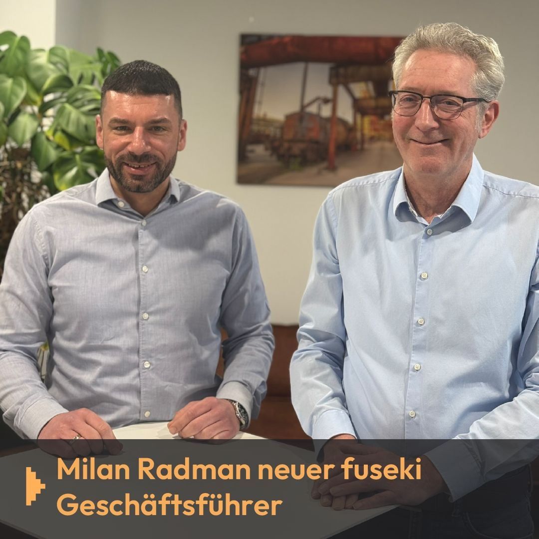Zwei Männer an einem Tisch, Text „Milan Radman neuer fuseki Geschäftsführer“
