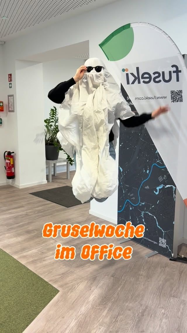 Person im weißen Gespensterkostüm mit Sonnenbrille im fuseki-Büro, Schriftzug „Gruselwoche im Office“